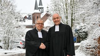 Pastor Ulrich Pohl und Pastor Bartolt Haase schütteln sich die Hände vor der verschneiten Zionskirche.