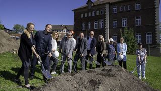 Gruppe von Menschen steht vor einem Erdhaufen und schaufelt Erde als symbolischen Spatenstich.