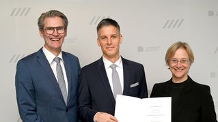 Zwei Männer und eine Frau lächeln in die Kamera