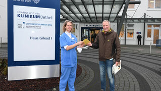 Ulrike Graulich nimmt von Matthias Jaene vor dem Eingang des EvKB die Gutscheine entgegen