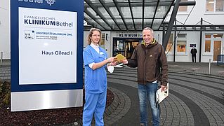 Ulrike Graulich nimmt von Matthias Jaene vor dem Eingang des EvKB die Gutscheine entgegen
