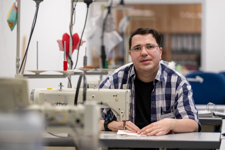 Matthias Schütze sitzt an der Nähmaschine und schaut in die Kamera