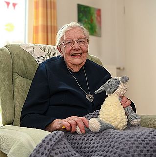 Diakonisse Gerda Hegemann sitzt mit ihrem Kuscheltier-Schaf im Sessel.