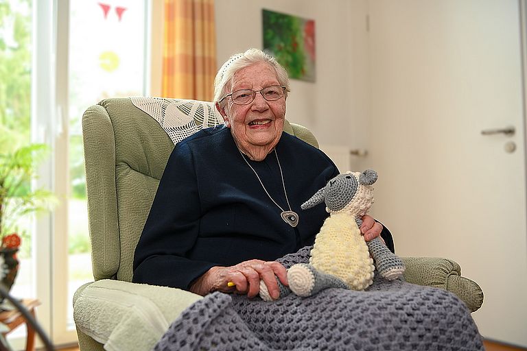 Diakonisse Gerda Hegemann sitzt mit ihrem Kuscheltier-Schaf im Sessel.