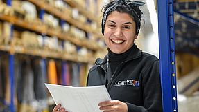 Woman stands leaning against a shelf in a large warehouse.