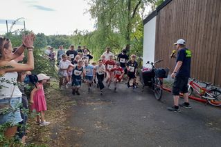 Kinder laufen beim Volkslauf mit, Erwachsene und ein Moderator feuern die Läufer an.