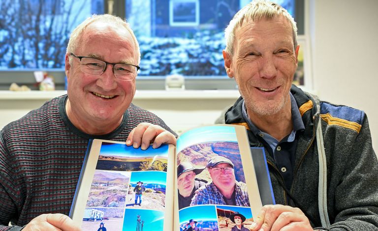 Frank Mintz und Rainer Haarmann halten ein Fotoalbum mit Bildern von ihrer USA Reise hoch und lächeln.