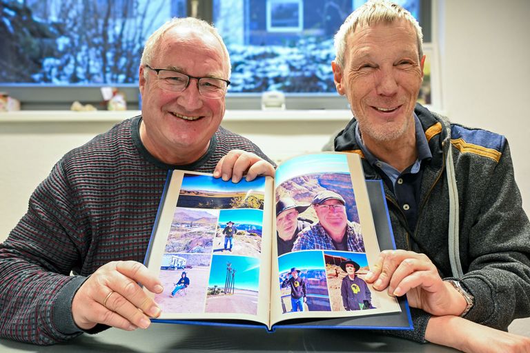 Frank Mintz und Rainer Haarmann halten ein Fotoalbum mit Bildern von ihrer USA Reise hoch und lächeln.