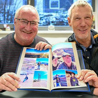 Frank Mintz und Rainer Haarmann halten ein Fotoalbum mit Bildern von ihrer USA Reise hoch und lächeln.