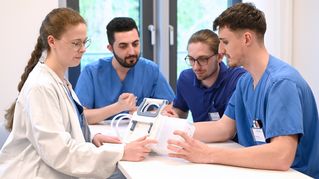 Eine Gruppe junger Menschen sitzt an einem Tisch in ihrer Krankenhauskleidung und bespricht sich.