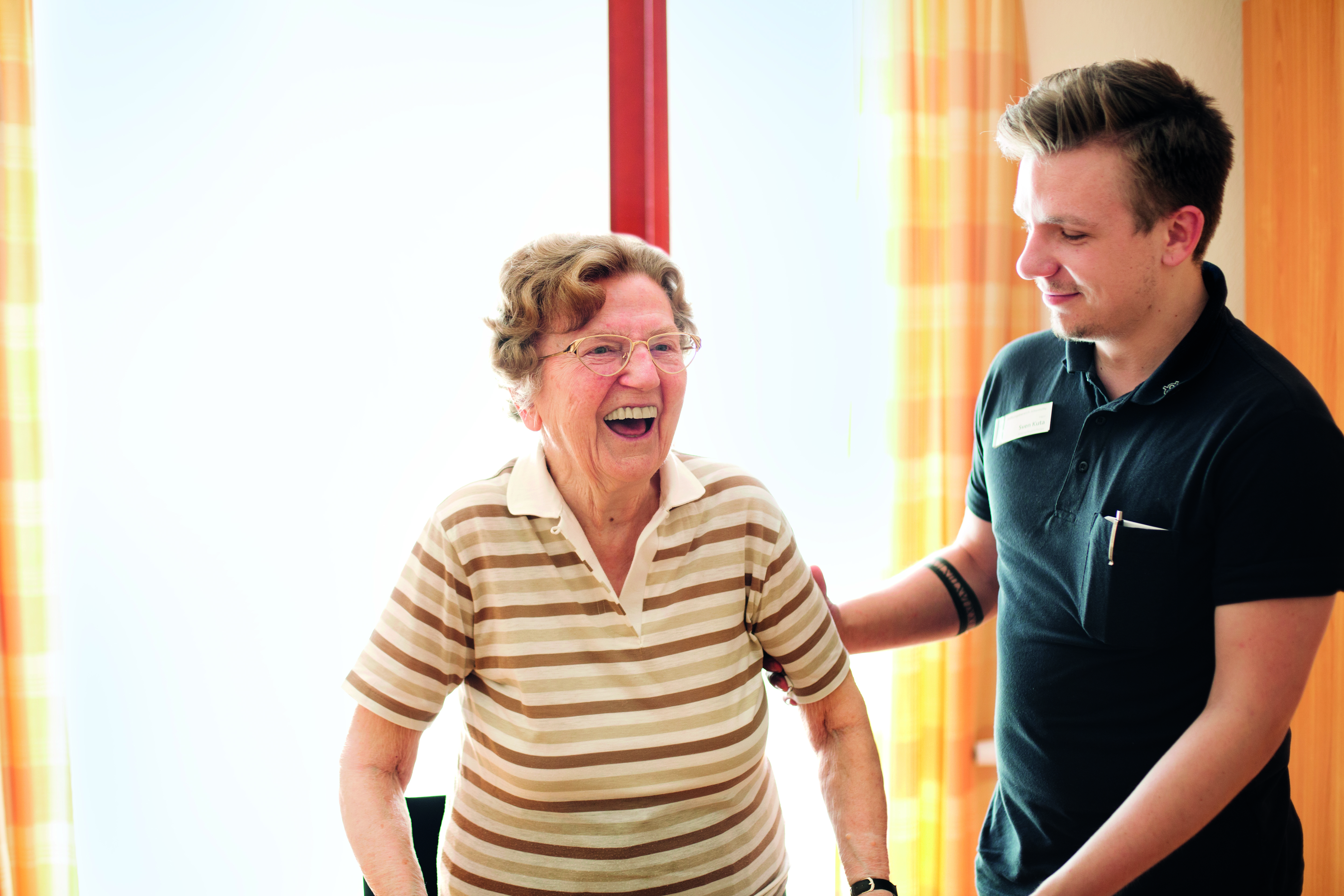 Ein Pfleger stützt eine lachende, ältere Frau